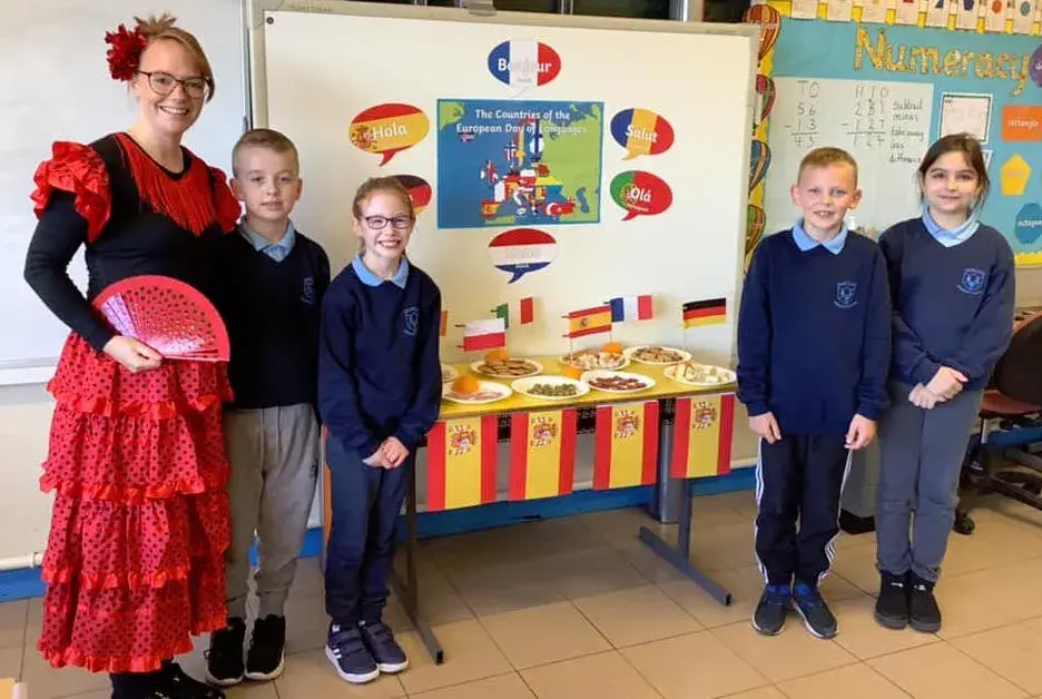 Dunclug PS - European Day of Languages - 4 children in Dunclug PS uniform with a teacher dressed in a Spainish dress with a modern languge display behind them