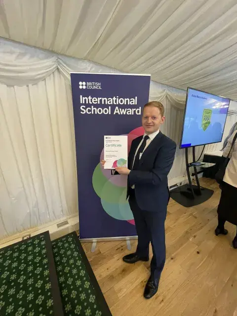 Dunclug PS Principal holding Award standing in front of a British Council pop up