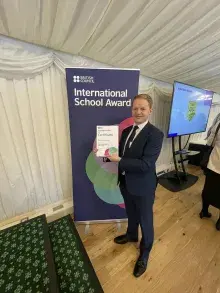 Dunclug PS Principal holding Award standing in front of a British Council pop up