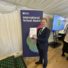 Dunclug PS Principal holding Award standing in front of a British Council pop up